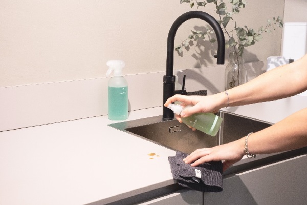 mujer utilizando un spray para limpiar la mesada de la cocina