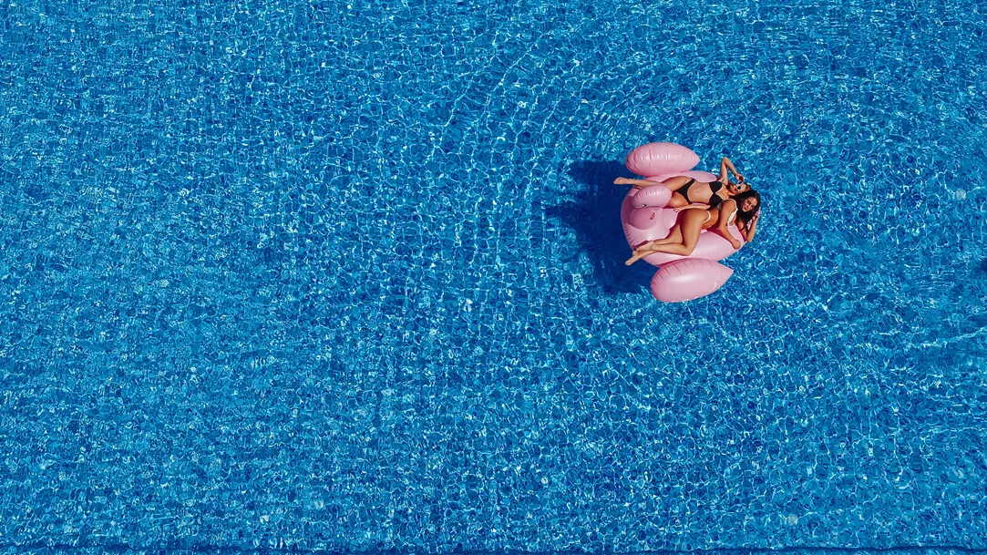 Vista áerea de dos mujeres jóvenes en una piscina sobre unos flamingos de plástico